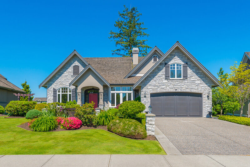 a well maintained front yard of suburban house with green grass, couple of trees and various planted bushes